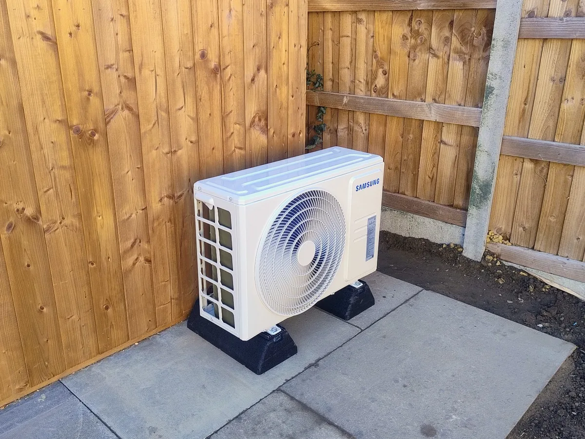 Samsung outdoor condenser on raised anti-vibration supports beside wooden fencing